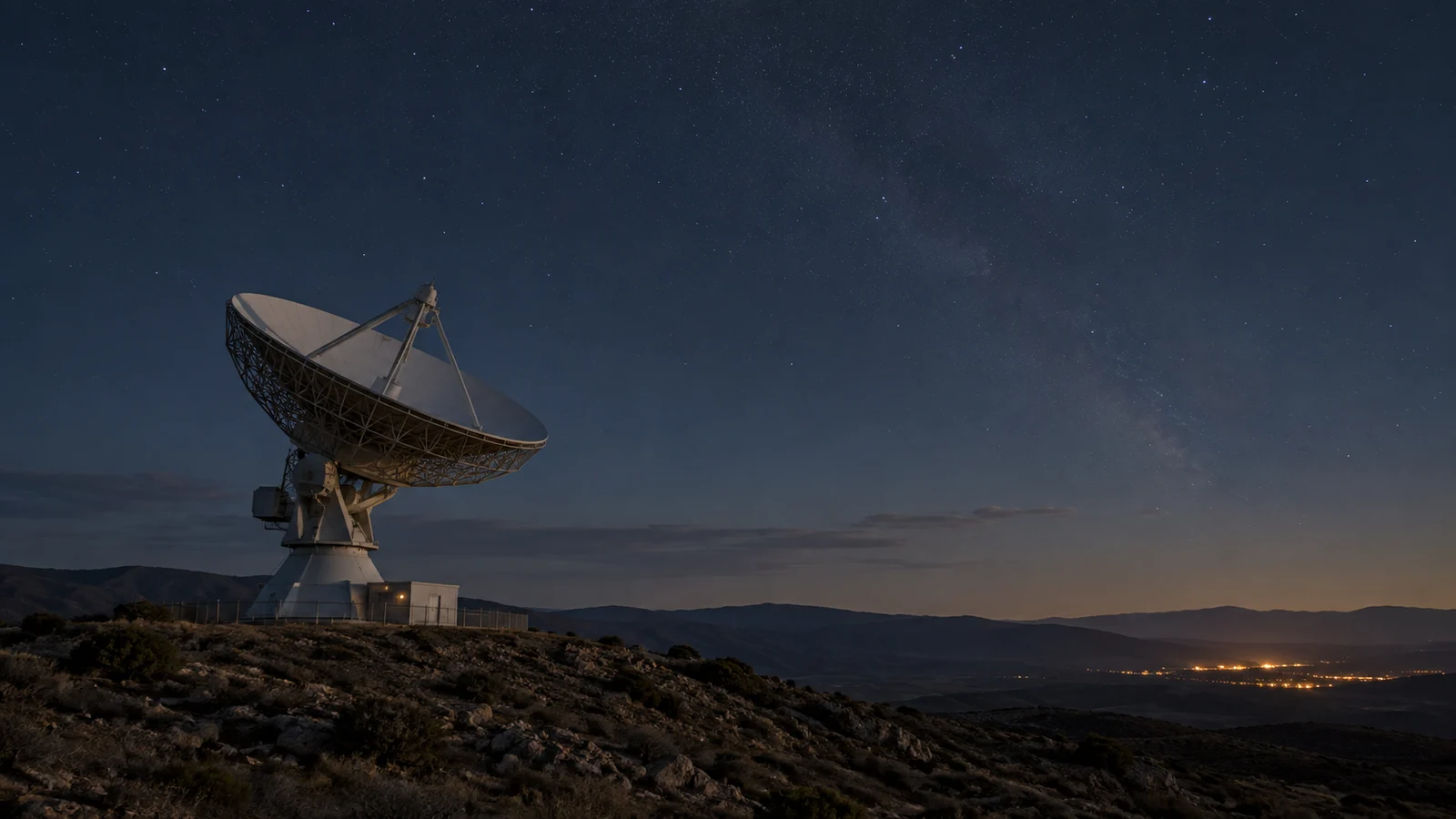 Un radiotelescopio en una loma bajo el cielo estrellado, con las luces de una población en el horizonte. Imagen generada.